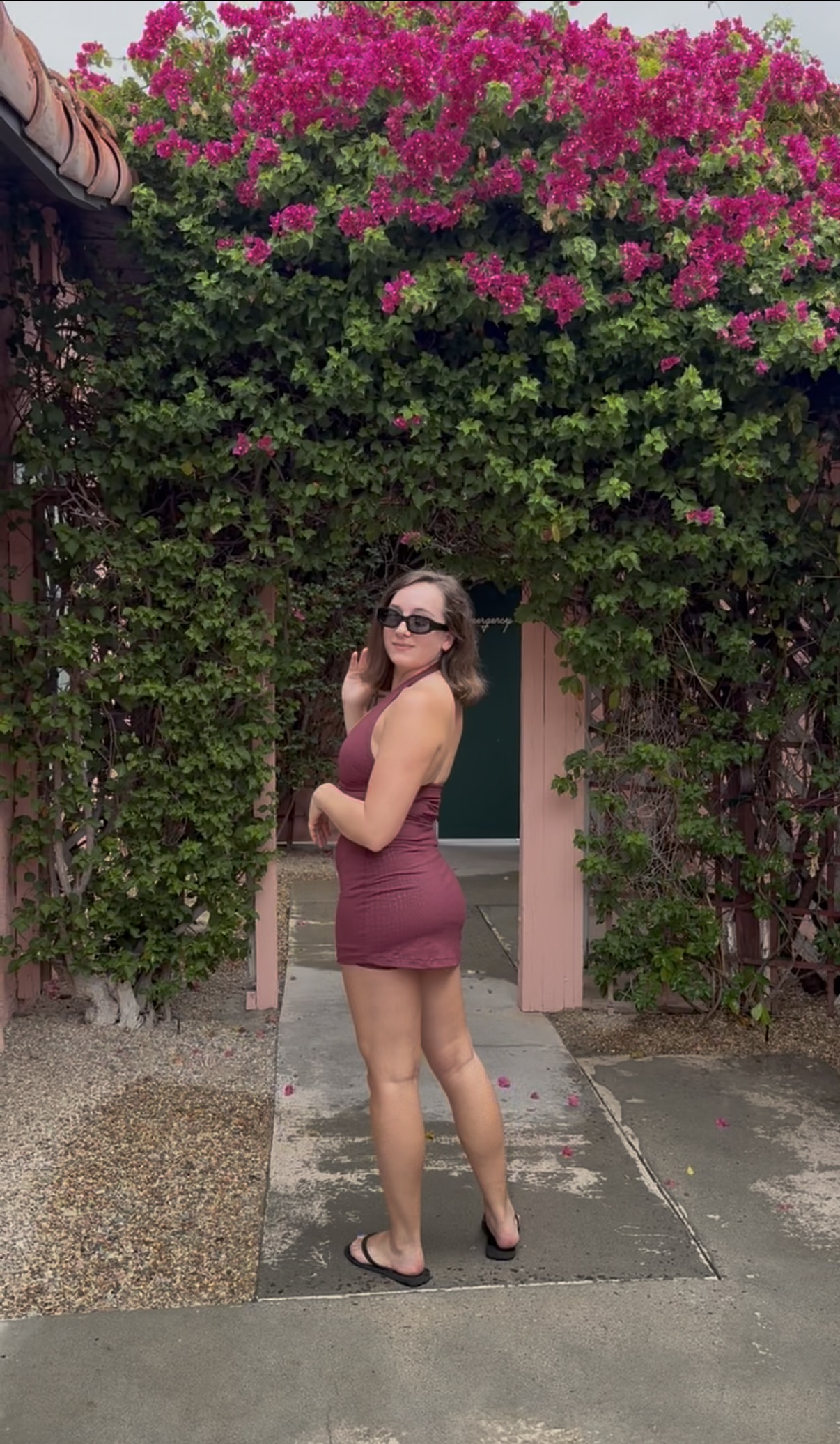Emily looking back over her shoulder in the Becky set, standing in front of a bougainvillea-covered archway, showing the low back of the halter top